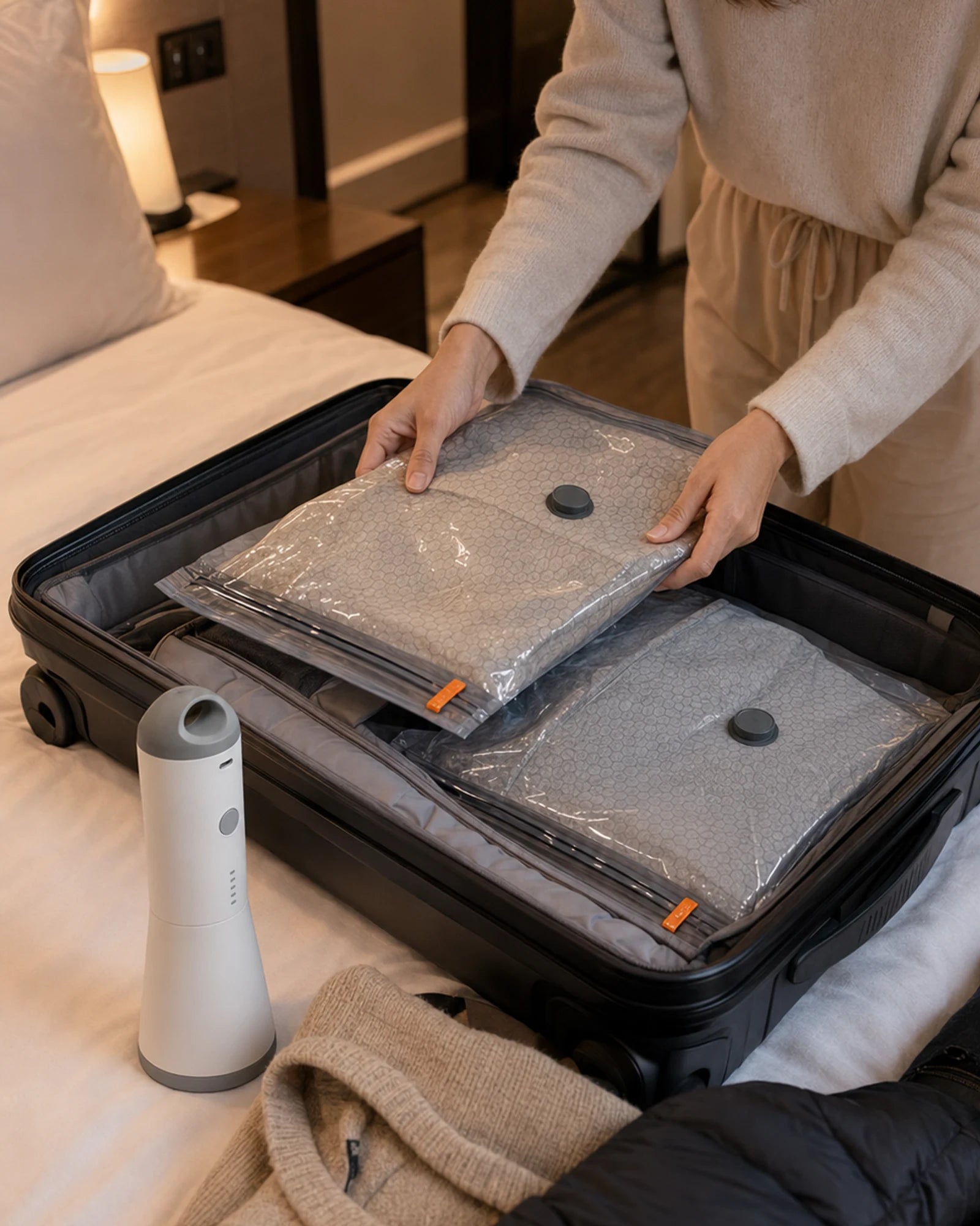 Traveler arranging filled gray compression bags in an open suitcase on a bed, with the SG-508 pump nearby.
