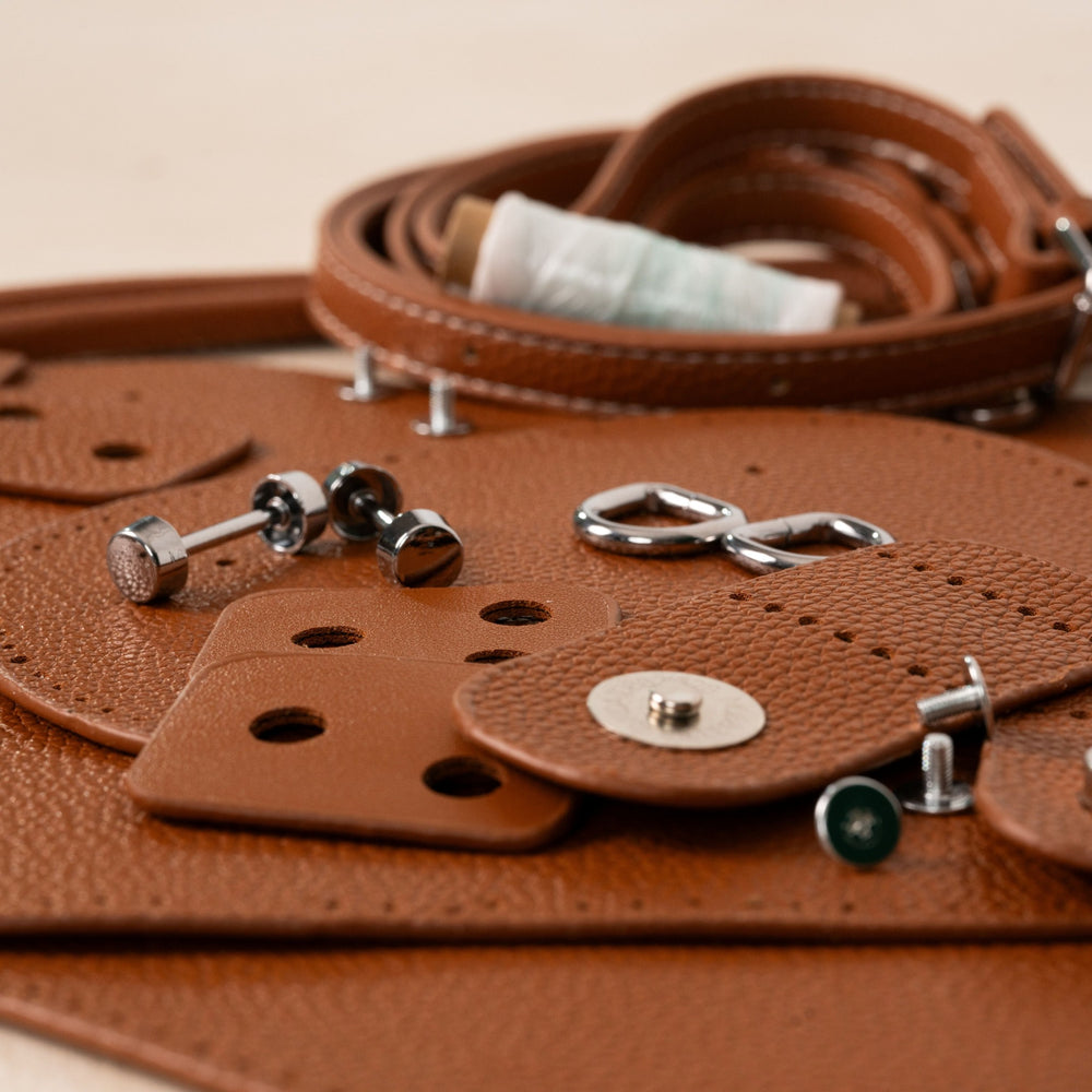 Brown handbag kit panels, straps, thread, and hardware arranged for assembly