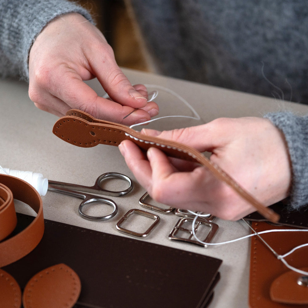 Hands stitching a brown handbag strap piece